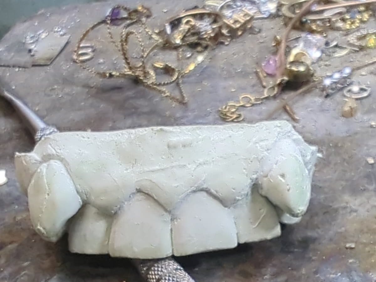 A model of a customer's teeth on our jeweler's bench, surrounded by gold pieces and a hand tool