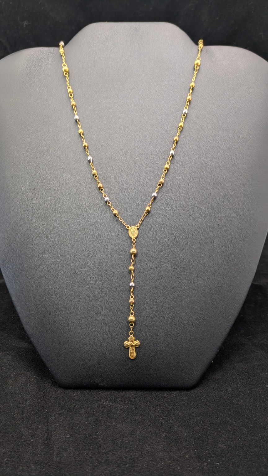 22-inch 14K rosary-style necklace with yellow and white-tone beads, oval centerpiece and crucifix drop on a dark jewelry display