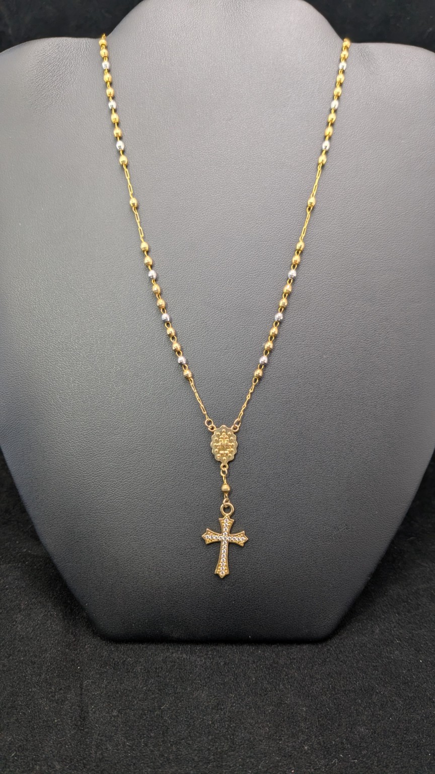 14K tri-color rosary-style necklace with faceted tri-color beads, decorative center and cross drop on a dark jewelry display