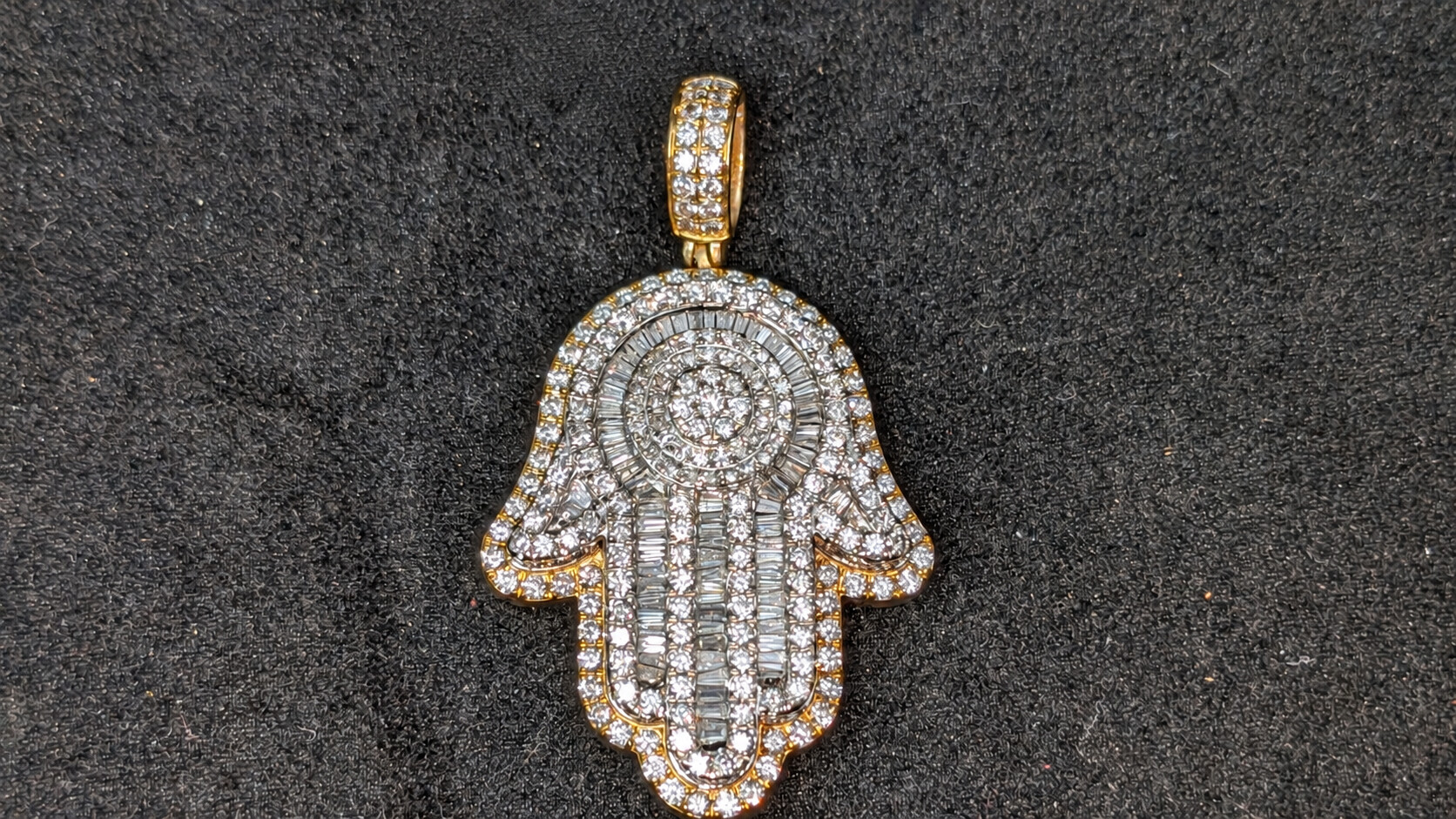 Hamsa hand pendant with rows of round and baguette diamonds on a dark jewelry display